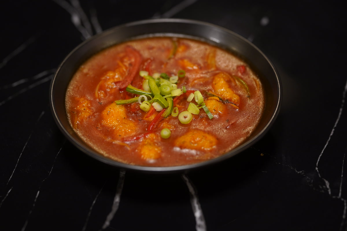 Signature red prawn curry topped with spring onions, on dark marble